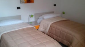 Habitación de hotel con dos camas, cada una con una colcha beige acolchada y almohadas. Entre las camas, una mesita de noche con una lámpara.