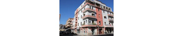 A multi-story building with balconies, a ground-floor shop, and a clear blue sky.