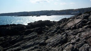 A rocky shoreline with a view of the sea and distant buildings. - The Falls at Ogunquit Resort, Maine (Ogunquit)