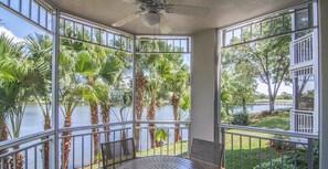 A room with large windows overlooking a lake, surrounded by palm trees, and featuring a ceiling fan and a round table with chairs. - Cypress Harbour Orlando Premium 2 Bedroom/2 Bath Villa - New Year's Week (Orlando)