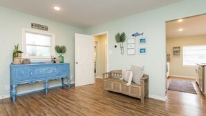 A spacious living room with hardwood flooring, a blue console table, a wooden bench with cushions, and a door leading to another room. - FAMILY FRIENDLY-CLOSE TO BEACH/DT 3 Bed/3 Bath (Rockport)