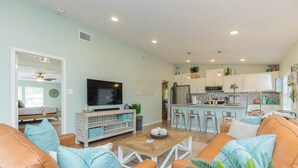 A modern living room with a sofa, coffee table, and TV. A kitchen with bar stools and a dining area is visible in the background. - FAMILY FRIENDLY-CLOSE TO BEACH/DT 3 Bed/3 Bath (Rockport)