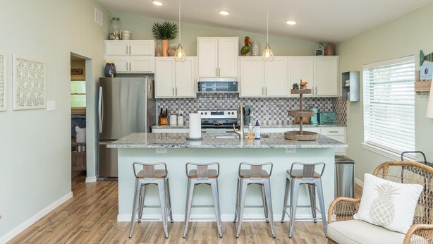 A modern kitchen with white cabinets, a central island with bar stools, and a dining area with a wicker sofa. - FAMILY FRIENDLY-CLOSE TO BEACH/DT 3 Bed/3 Bath (Rockport)