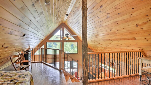 Ein gemütliches Schlafzimmer im Dachgeschoss mit Holzbalkendecke, einem großen Fenster, einem Bett und einer Treppe, die auf einen Balkon führt.