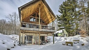 Eine zweistöckige Holzhütte mit Balkon, umgeben von Schnee und Bäumen.