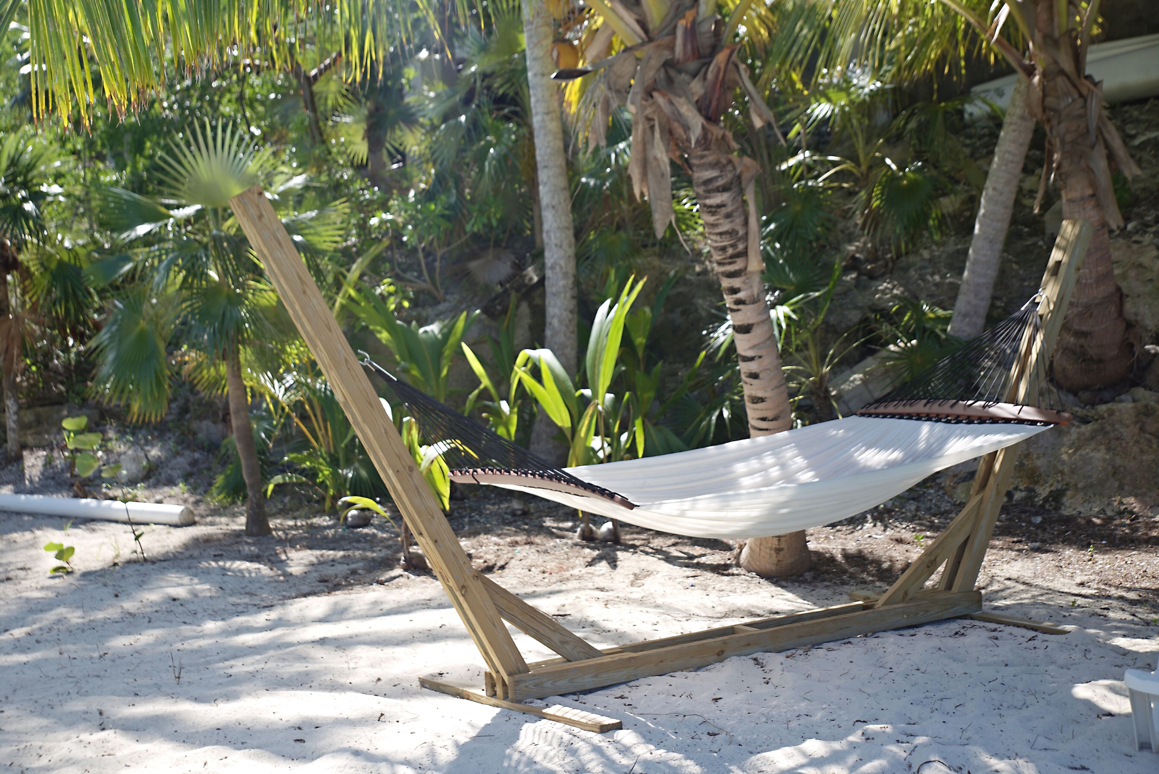 Een hangmat op een zanderig strand, met palmbomen op de achtergrond.