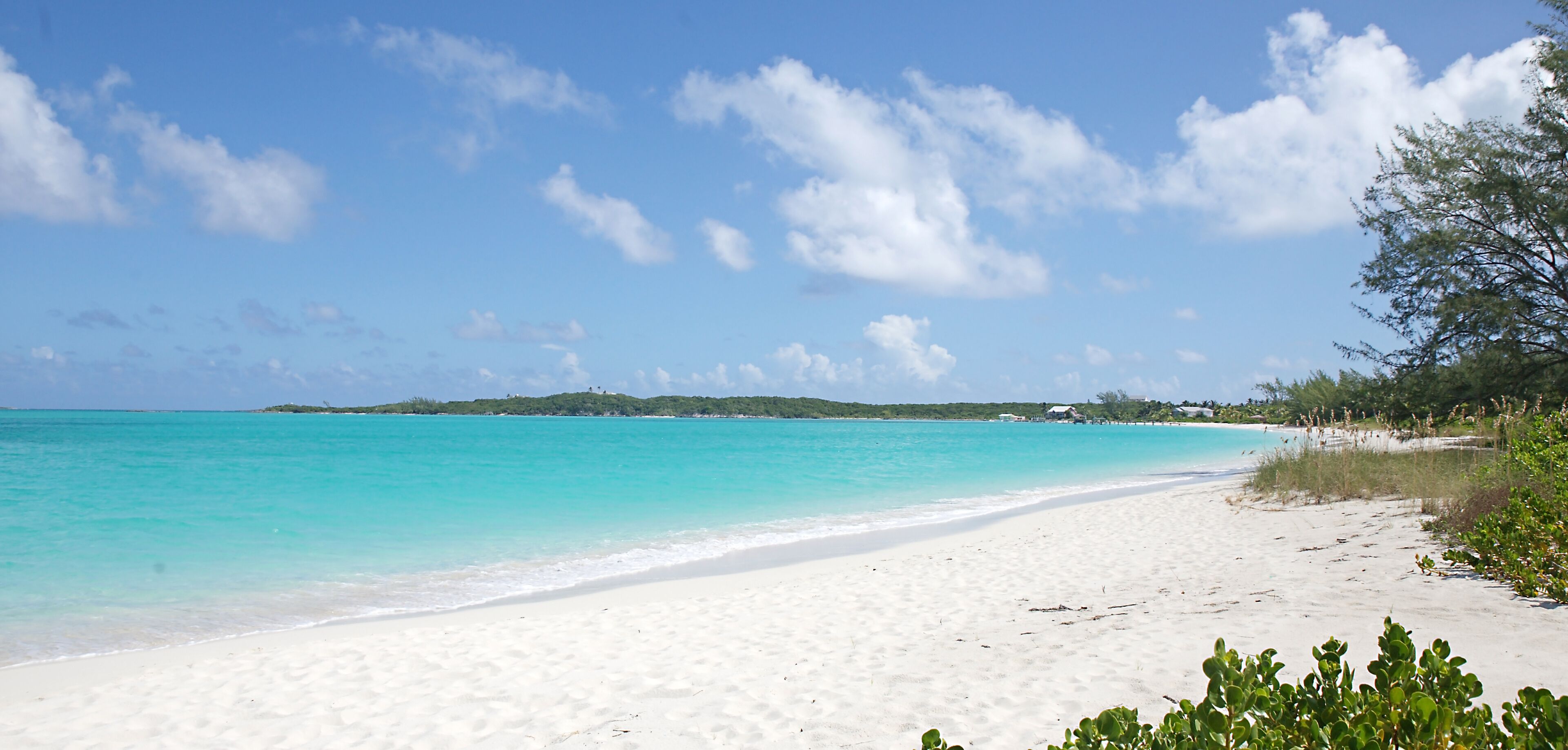A beach with clear turquoise water, white sand, and a distant tree-covered island.