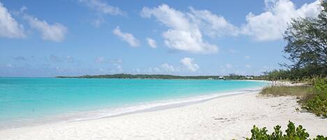 A beach with clear turquoise water, white sand, and a distant tree-covered island.
