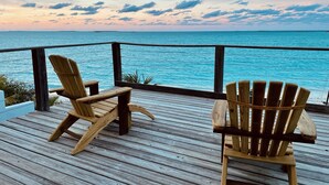 Un pontile di legno con due poltrone Adirondack rivolte verso un mare turchese al tramonto.