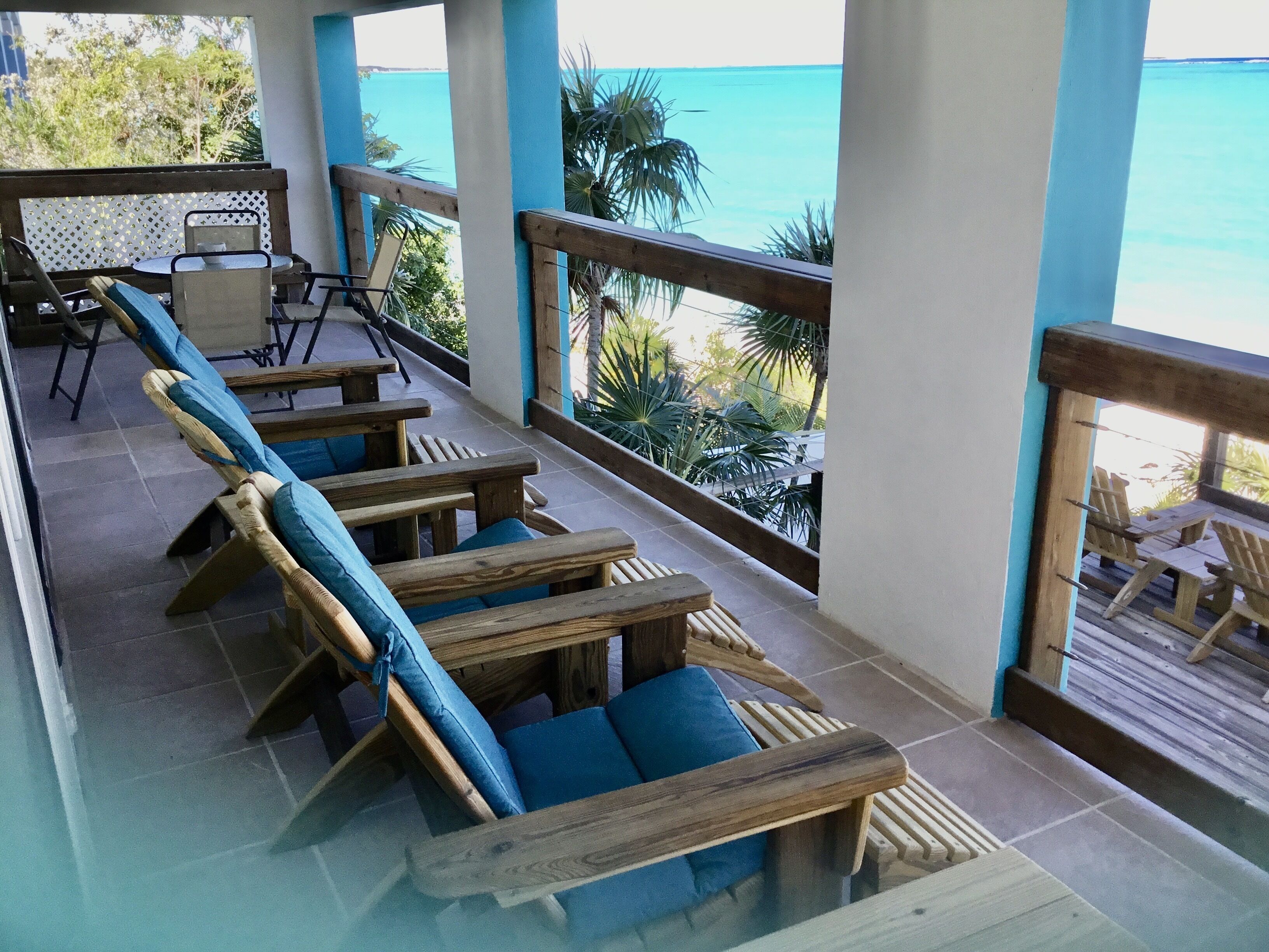 Een houten terras met blauwe fauteuils, uitkijkend op een turquoise zee.