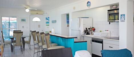 A modern kitchen with white cabinets, a blue countertop, and a dishwasher. There are two blue chairs and a white trash bin.