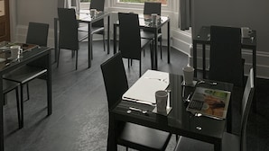 Een eetgedeelte met tafels en stoelen, grote ramen met uitzicht op zee, en kunstwerken aan de muren.