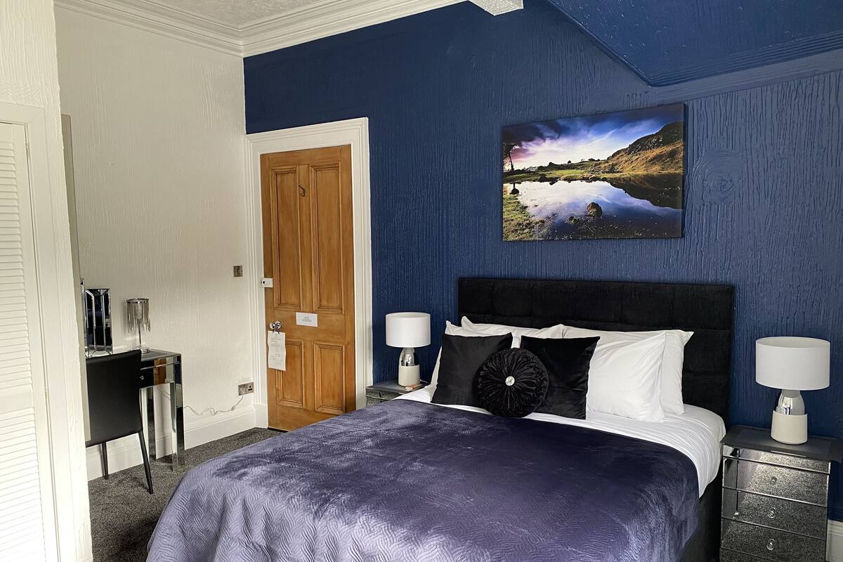 Een slaapkamer met een bed, twee nachtkastjes, een deur en een aan de muur hangend schilderij.