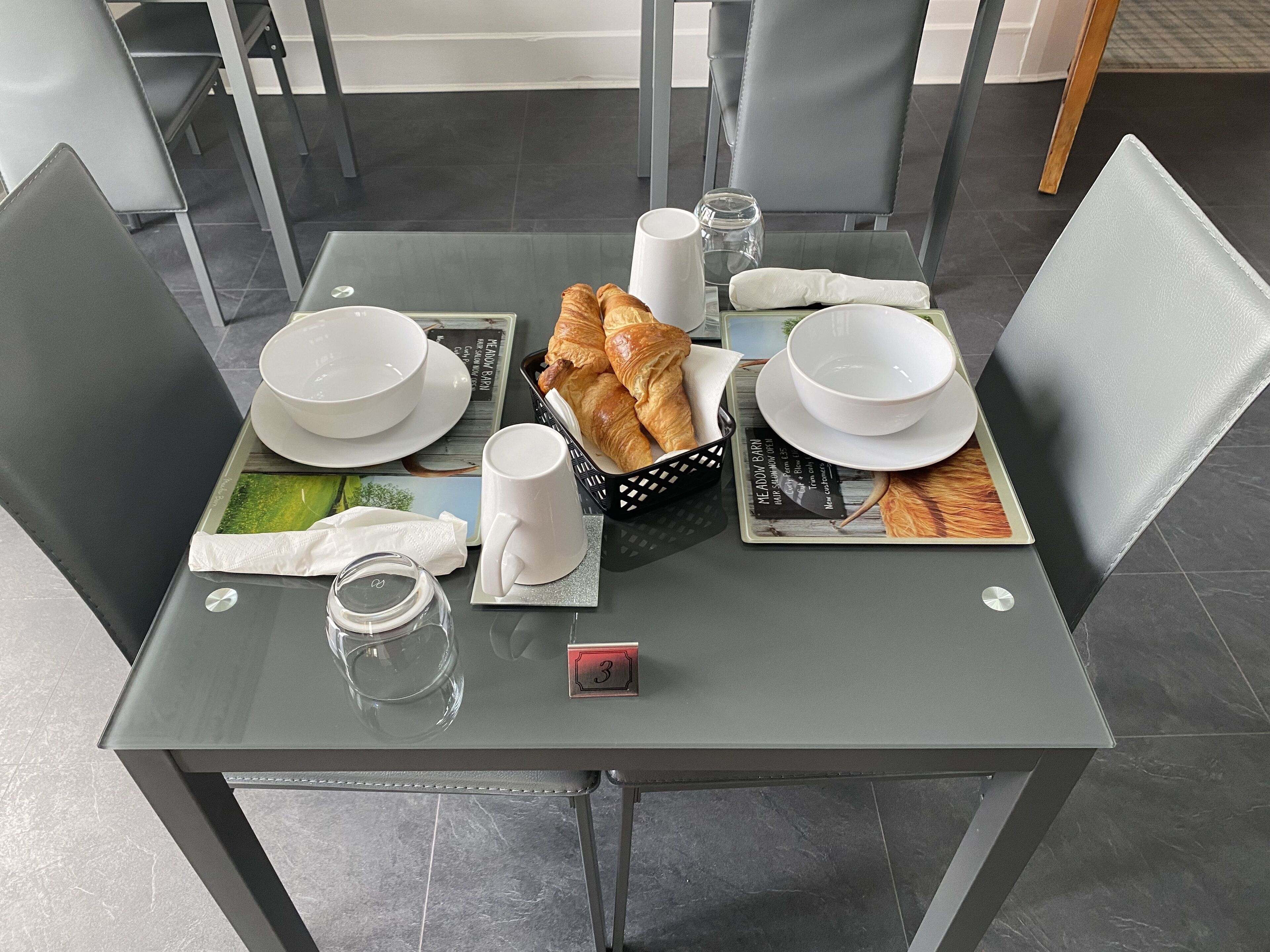 A table set for breakfast with croissants, coffee cups, and a menu.