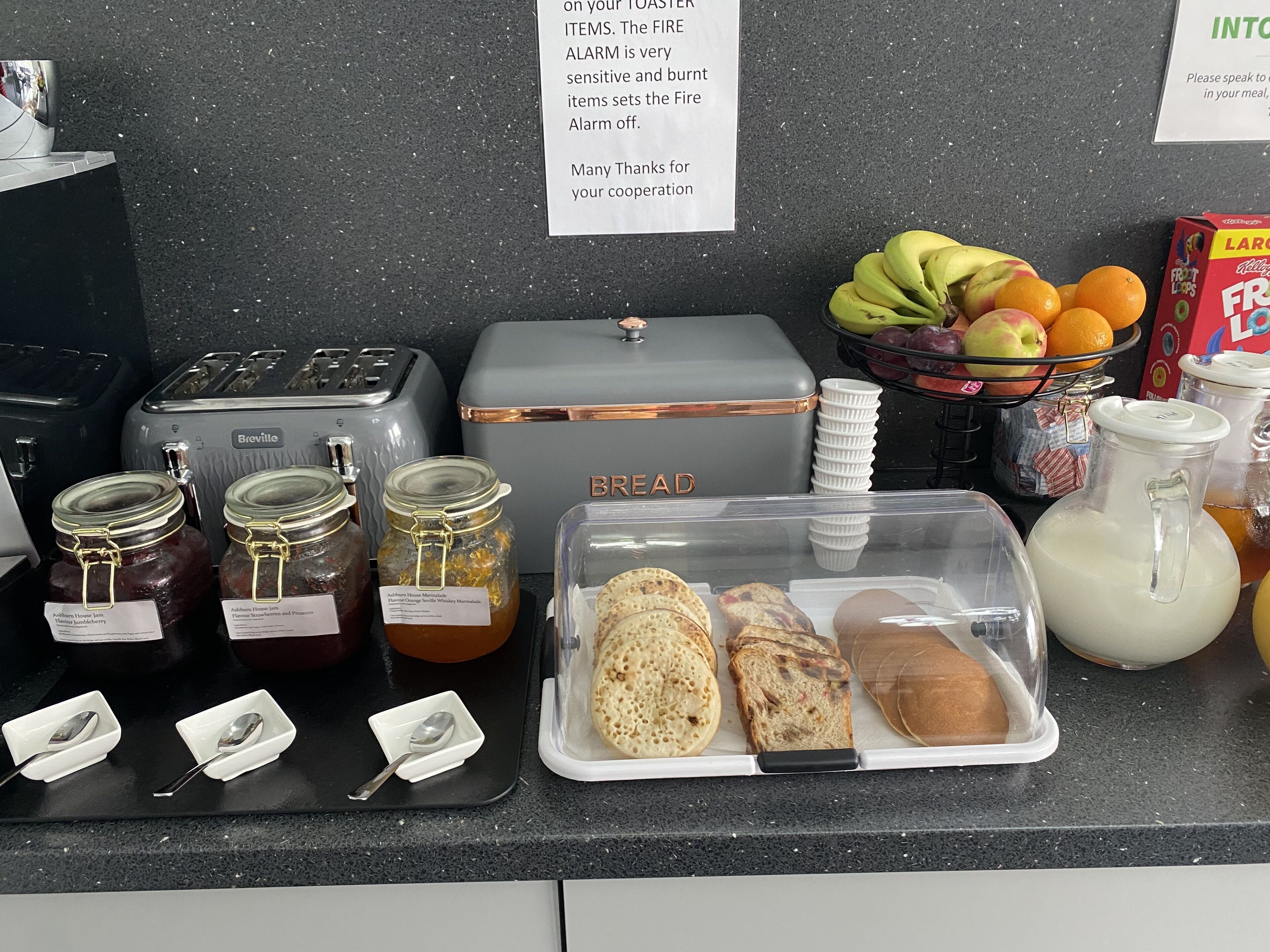 A breakfast counter with Breville appliances, jars of jam, bread, and a fruit bowl.