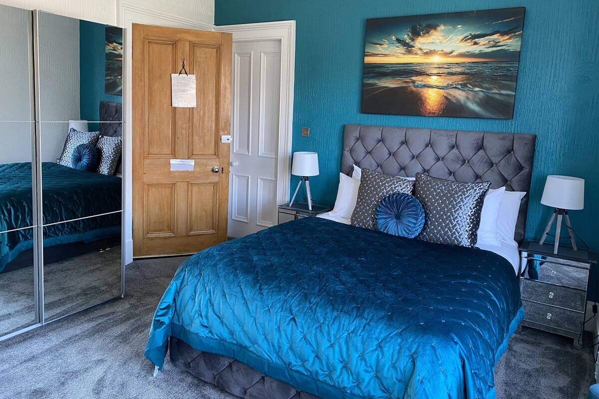 Een slaapkamer met een groot bed, een spiegel, een deur en een schilderij van een ondergaande zon.