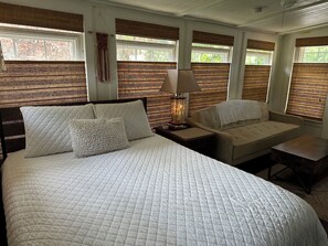 Une chambre à coucher avec un grand lit, une table de chevet avec une lampe, un canapé et une fenêtre avec des stores.