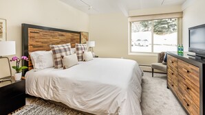 A modern bedroom with a large bed, wooden headboard, and a television on a dresser. - Dog Friendly Aspen Alps Condo walking distance to town with Pool (Aspen)