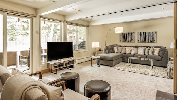A spacious living room with a large flat-screen TV, a grey sectional sofa, and a coffee table. There are two ottomans and a patterned rug on the floor. - Dog Friendly Aspen Alps Condo walking distance to town with Pool (Aspen)