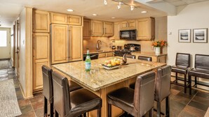 A kitchen with wooden cabinets, a granite countertop, a stainless steel refrigerator, and a microwave. There are four chairs around the counter and a sink. - Dog Friendly Aspen Alps Condo walking distance to town with Pool (Aspen)