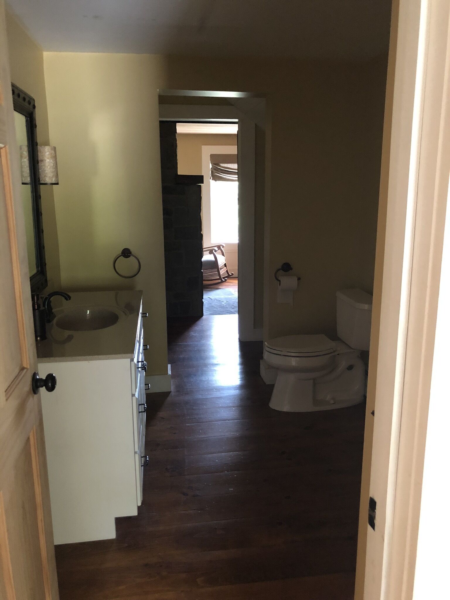 A narrow hallway with a wooden floor leading to a bathroom with a toilet and sink.