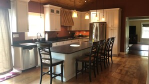 A kitchen with wooden cabinets, a stainless steel refrigerator, a large island with bar stools, and pendant lighting.
