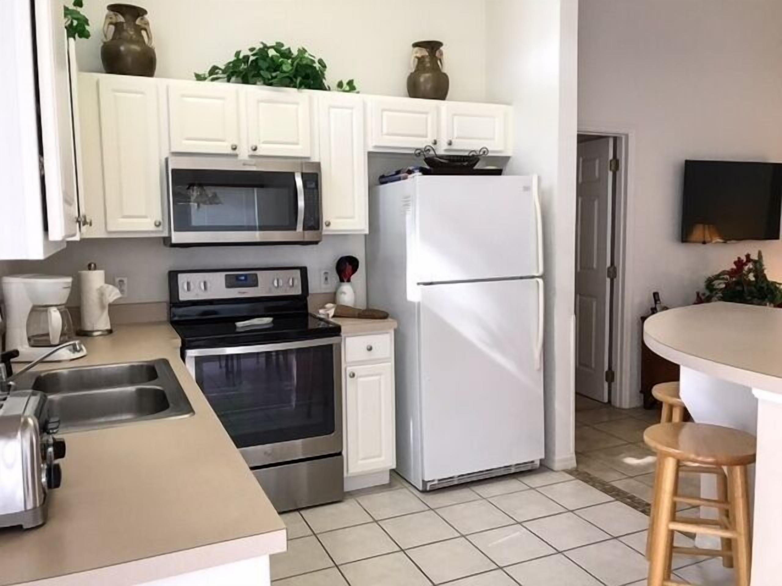 Una cocina moderna con gabinetes blancos, electrodomésticos de acero inoxidable, microondas, horno y refrigerador.