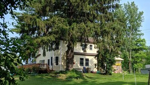 Uma casa de dois andares com uma árvore grande na frente, um pequeno alpendre e um gramado.