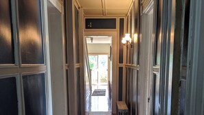 Um corredor com piso de madeira e detalhes brancos, que leva a uma porta com luminária acima.