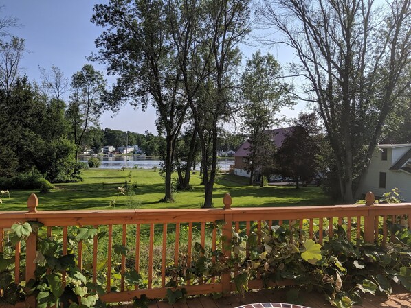 A view from a balcony with a wooden railing, overlooking a grassy area with trees and a body of water in the background. - Large docks, place for memories as one of a kind. Relax, play, swim, fish (Central Square)