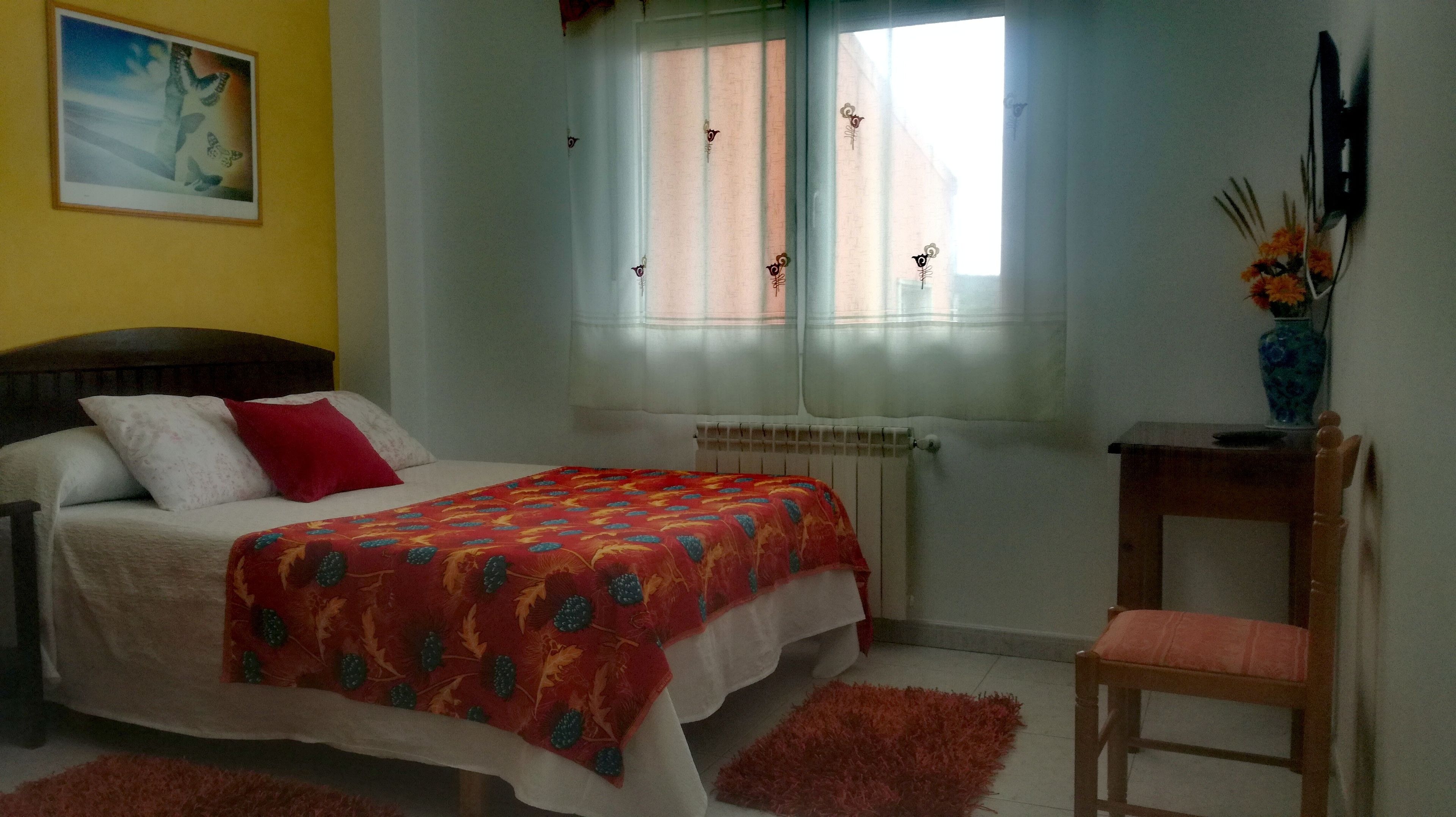 A bedroom with a bed, a chair, a radiator, and a window with curtains.