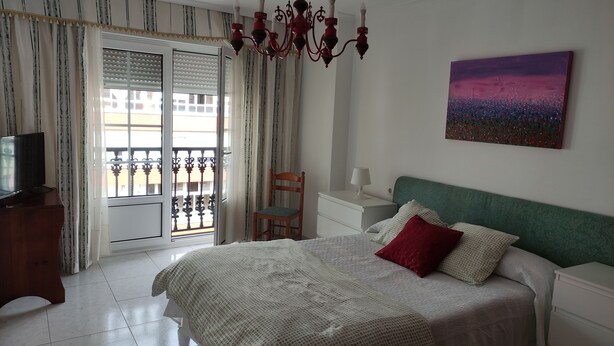 A bedroom with a bed, a chair, a nightstand, a TV, and a painting on the wall.