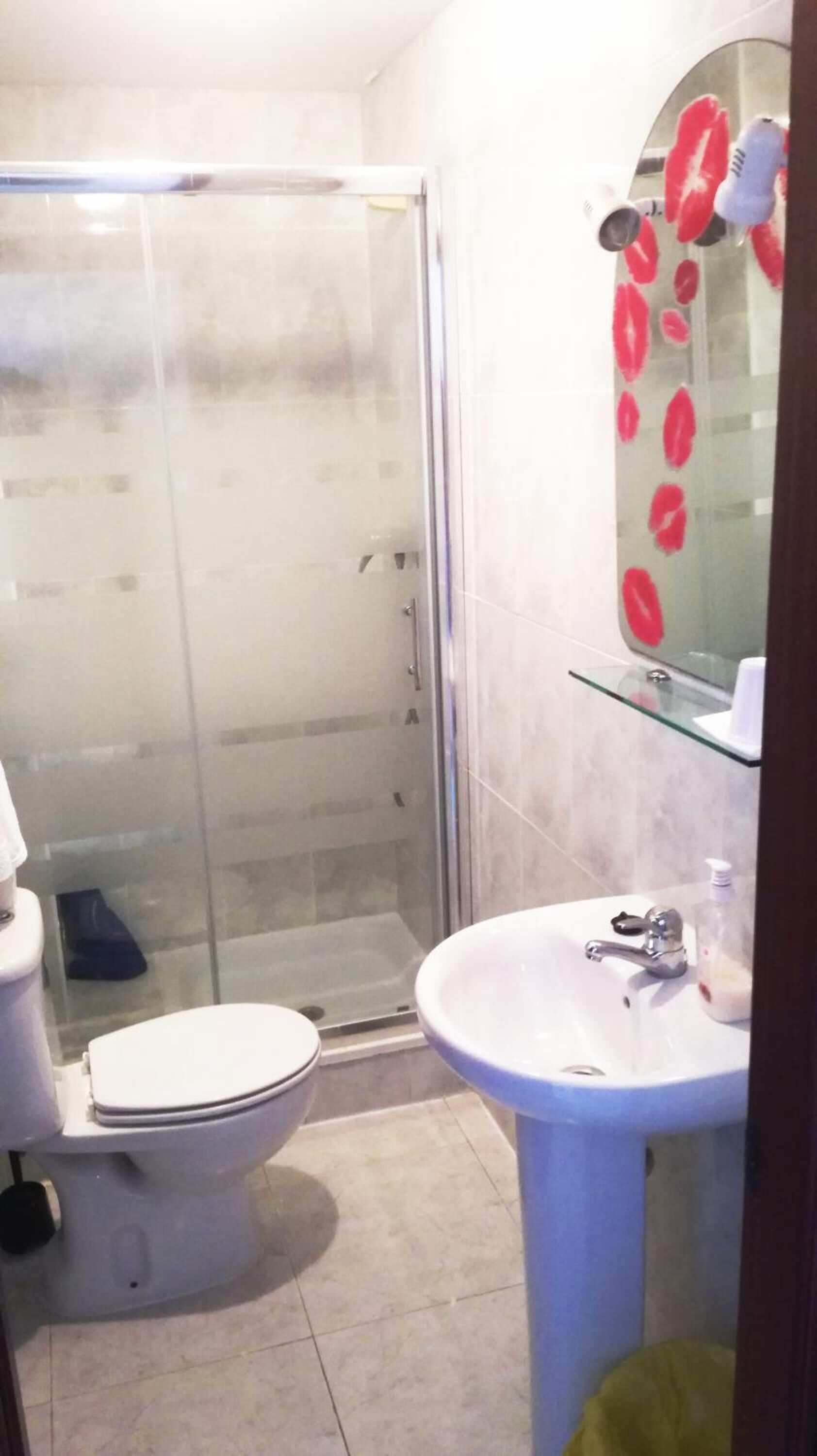 A bathroom with a glass shower enclosure, a toilet, and a sink with a mirror above it.