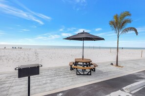 Una mesa de picnic junto a la playa, con toldo, una parrilla y una palmera.