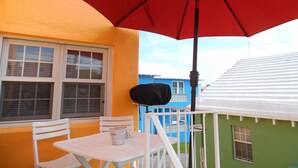A balcony with a white table and chairs, a red umbrella, and a view of colorful buildings.