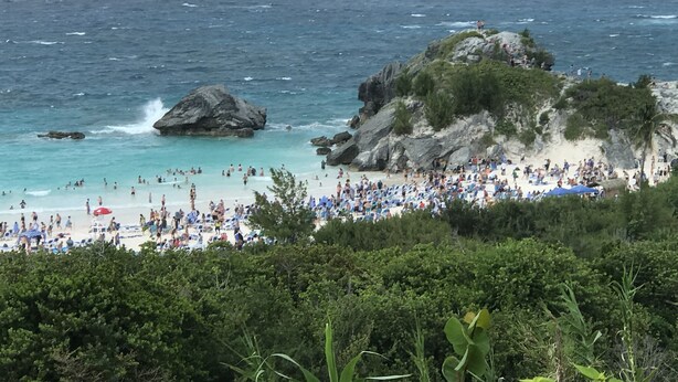A beach with people, a rocky outcrop, and the sea.