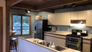 Eine moderne Küche mit Edelstahl-Kühlschrank, Mikrowelle und Herd, Holzschränken und einem großen Fenster mit Blick auf einen Garten.