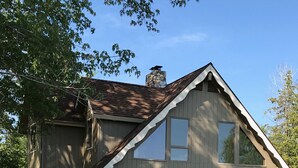 Ein zweistöckiges Haus mit einem Steinkamin, großen Fenstern und einer Veranda.