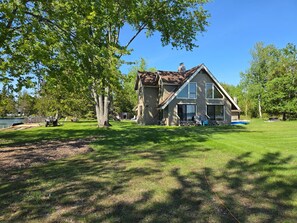 Une grande maison avec un toit en pente, une cheminée et une pelouse bien entretenue.