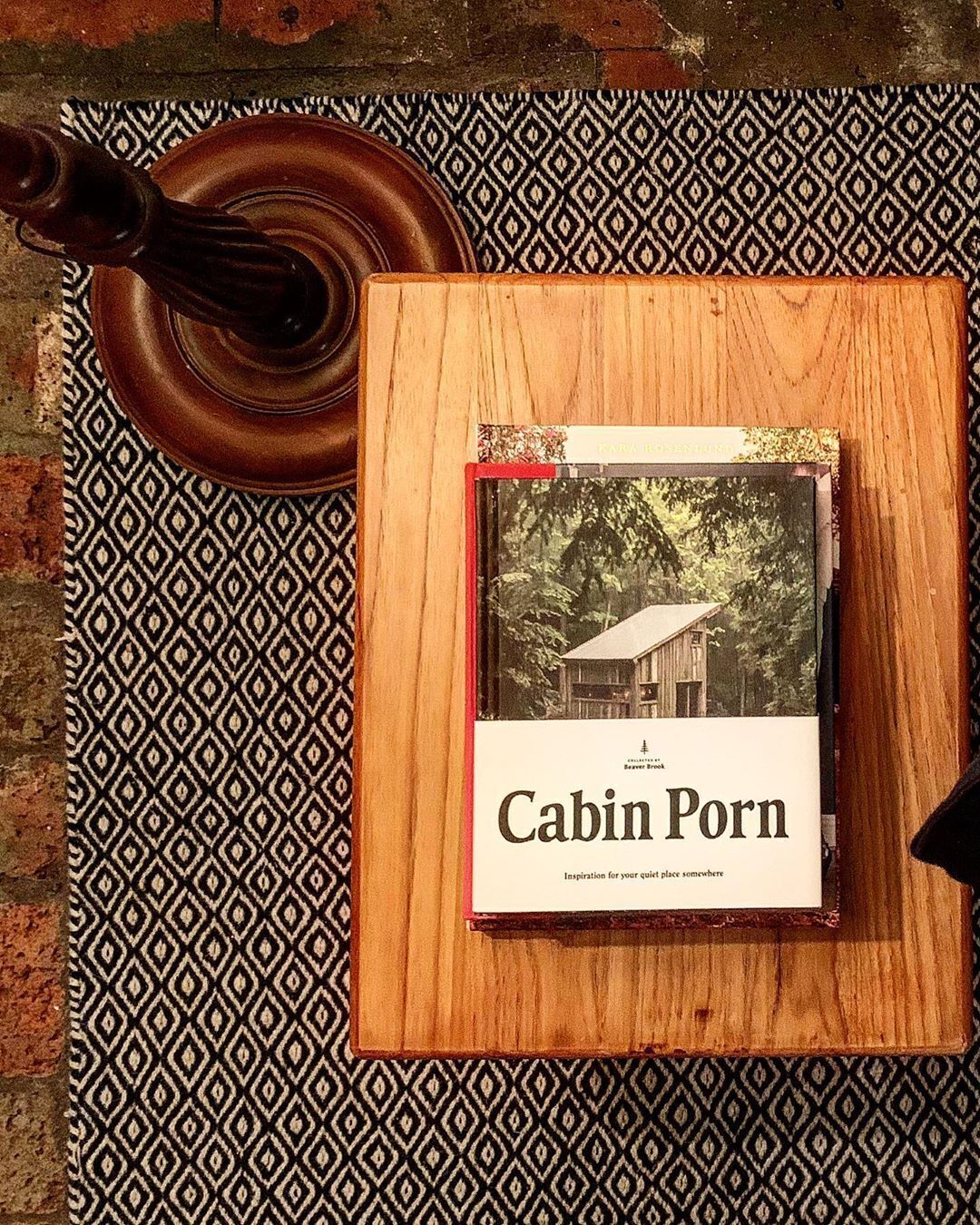 Un llibre anomenat 'Cabin Porn' sobre una superfície de fusta, sota la qual hi ha un estotxa amb un dibuix.