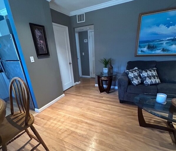 A living room with a dark-colored sofa, a glass coffee table, and a framed painting on the wall.
