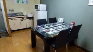 A compact kitchen with a microwave, a kettle, and a small refrigerator. A glass table with chairs is in the foreground. - Self-catering with Wi-fi and amenities. 10 minutes from JR Kasuga Station. MIYUKIHOUSE302 (春日市)