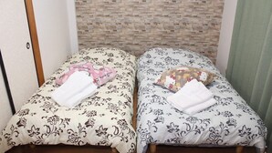 Two single beds with floral-patterned bedding, a wooden floor, and a brick-patterned wall behind them. - Self-catering with Wi-fi and amenities. 10 minutes from JR Kasuga Station. MIYUKIHOUSE302 (春日市)