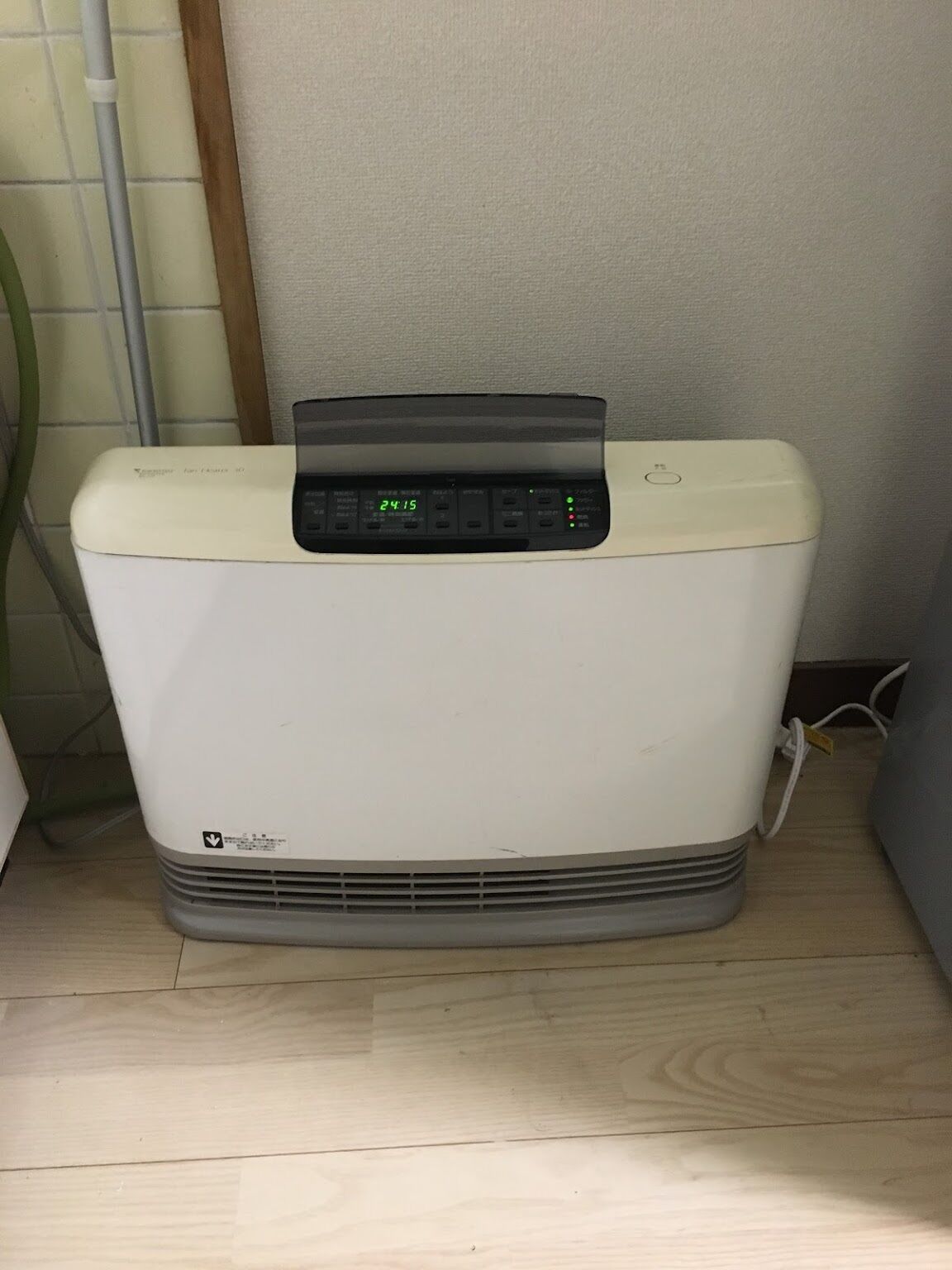 A portable heater with a digital display, placed on a wooden floor against a wall.