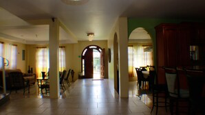 A spacious hallway with a dining area and kitchen on one side, and a living room on the other.