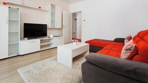 A modern living room with a flat-screen TV, white entertainment unit, and a grey sofa with red cushions. - Brasov Holiday Apartments -panoramic 10 (Brasov)