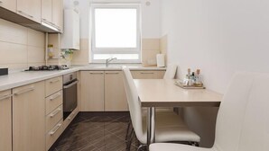 A modern kitchen with light-colored cabinets, a built-in oven, a sink, and a window providing natural light. - Brasov Holiday Apartments -panoramic 10 (Brasov)