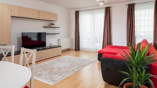 A modern living room with a flat-screen TV, a red sofa, a dining table with chairs, and a potted plant. - Brasov Holiday Apartments -panoramic 10 (Brasov)