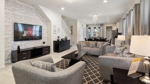 A modern living room with a flat-screen TV, grey sofas, a coffee table, and a staircase leading to another level. - Stunning 5bd Retreat, Pool, BBQ, PS5 & Game Room, Jnear Disney (Kissimmee)