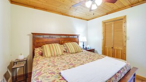 A bedroom with a wooden ceiling, a bed with floral bedding, a nightstand with a lamp, and a wooden wardrobe. - Secluded Lenoir Cabin: 4 Mi to Dtwn Blowing Rock (Lenoir)